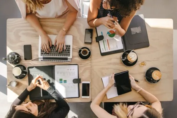 Top view of four women sitting around table in cafe with laptop, digital tablet and documents. Group of women working together in coffee shop. | Leading from the Front: WSP’s Women Leaders are Paving the Way to a More Equitable Future